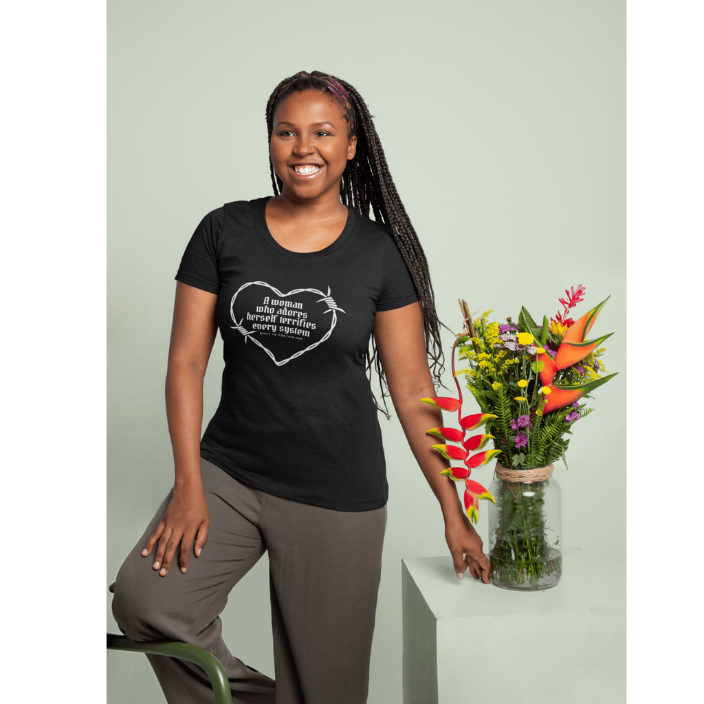 Woman wearing a black t-shirt with a design, standing next to a vase of flowers on a light green background