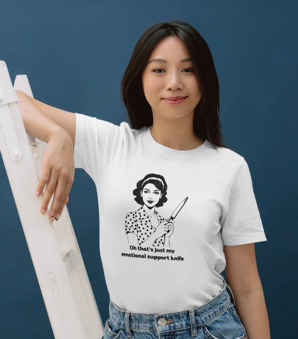 White  t-shirt featuring a vintage-style black line illustration of a 1950s housewife in a polka dot dress holding a large kitchen knife, with the text: “Oh that’s just my emotional support knife.”