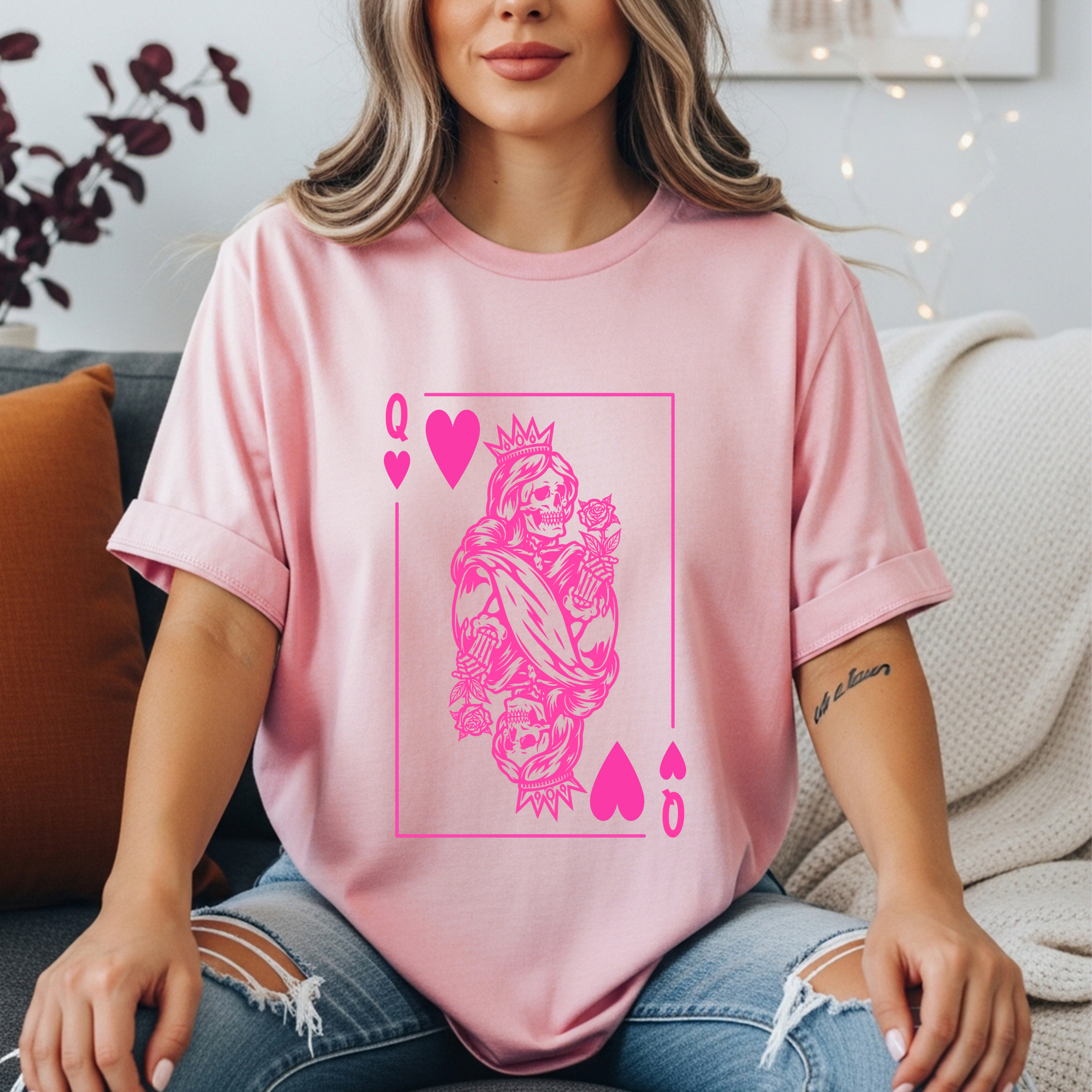 light pink graphic tee featuring a bold hot pink Queen of Hearts playing card design with a crowned skeleton queen, roses, and skulls. Edgy feminine shirt, skeleton queen tee, dark glam graphic shirt, witchy women’s gift, bold statement shirt for women